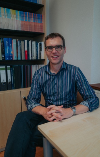 Prof. Clemens Wöllner sitzt am Schreibtisch in seinem Büro vor einer Bücherwand.